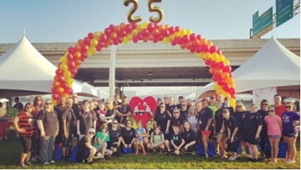 A large group of Kindred at Home associates underneath a colorful balloon arch, celebrating a 25th anniversary.