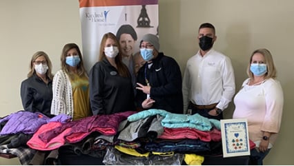 A small group of Kindred at Home associates wearing face masks and standing in front of a table piled with donated clothing.