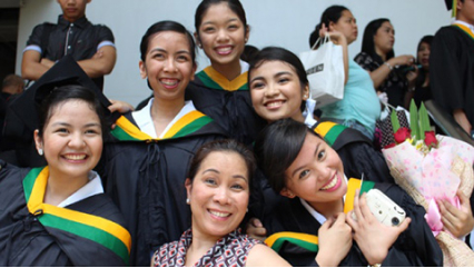 A small group of women dressed in college graduation robes, smiling and celebrating graduation day. 