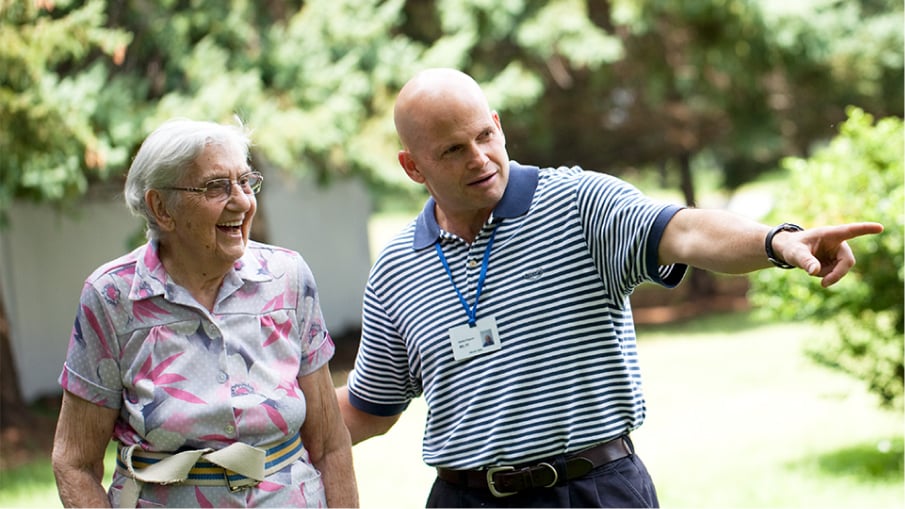 An elderly patient laughing and standing beside a caregiver.