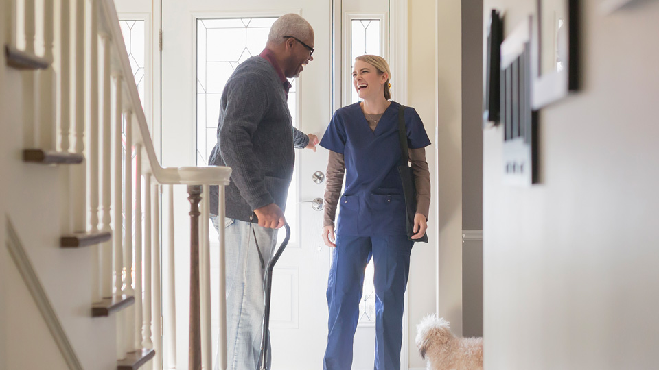 A patient smiling and greeting a nurse at the door of his home. 