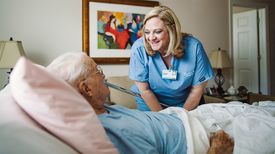 A hospice nurse smiling and speaking with a patient.