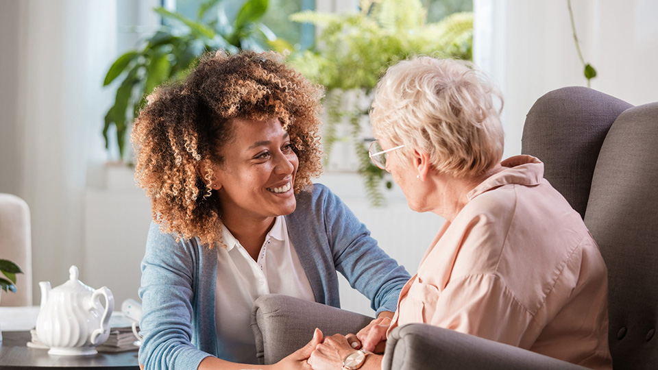 A personal home caregiver smiling and holding hands with a patient.