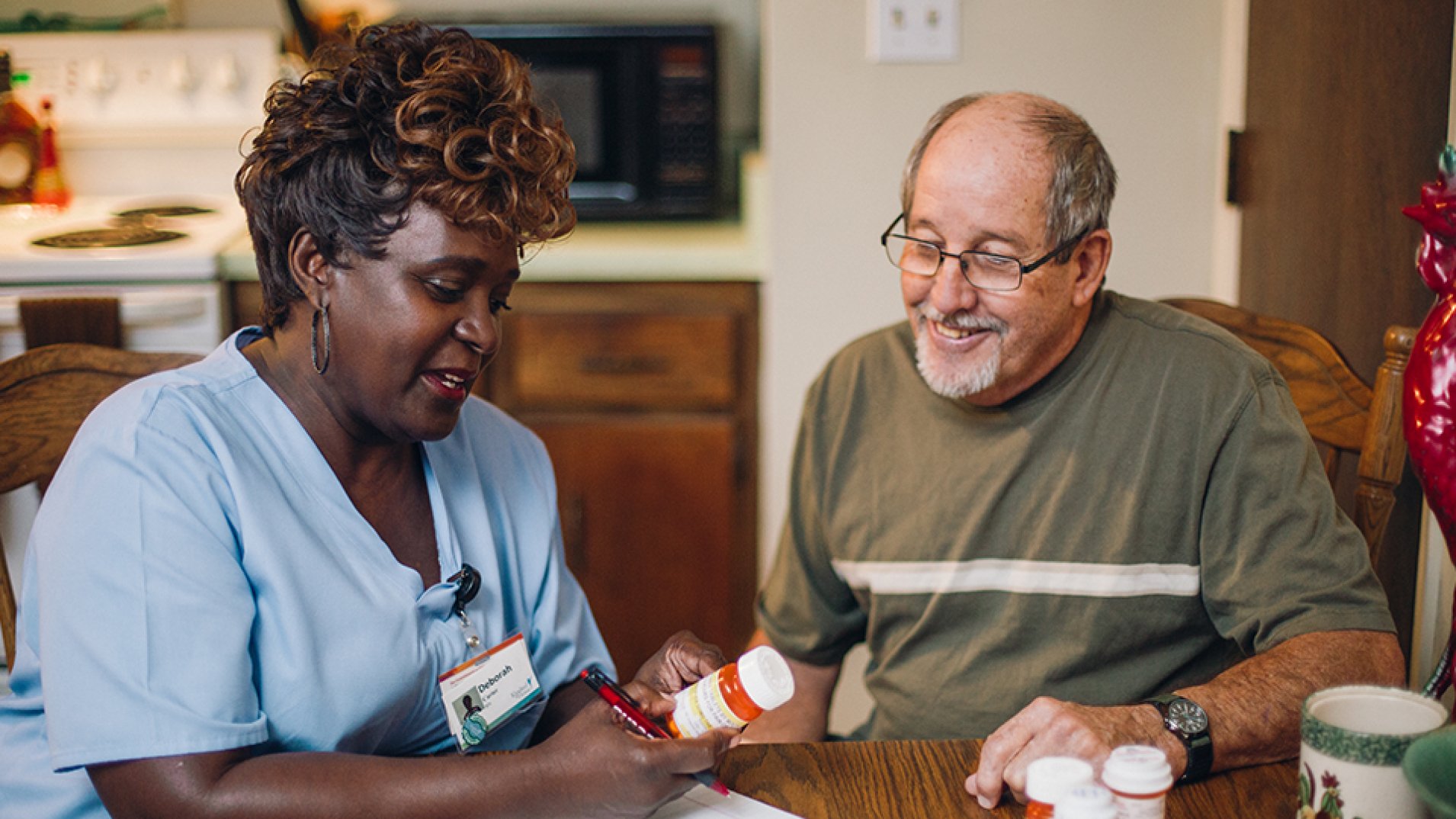 A home caregiver explaining the information on a pill bottle to a smiling patient.