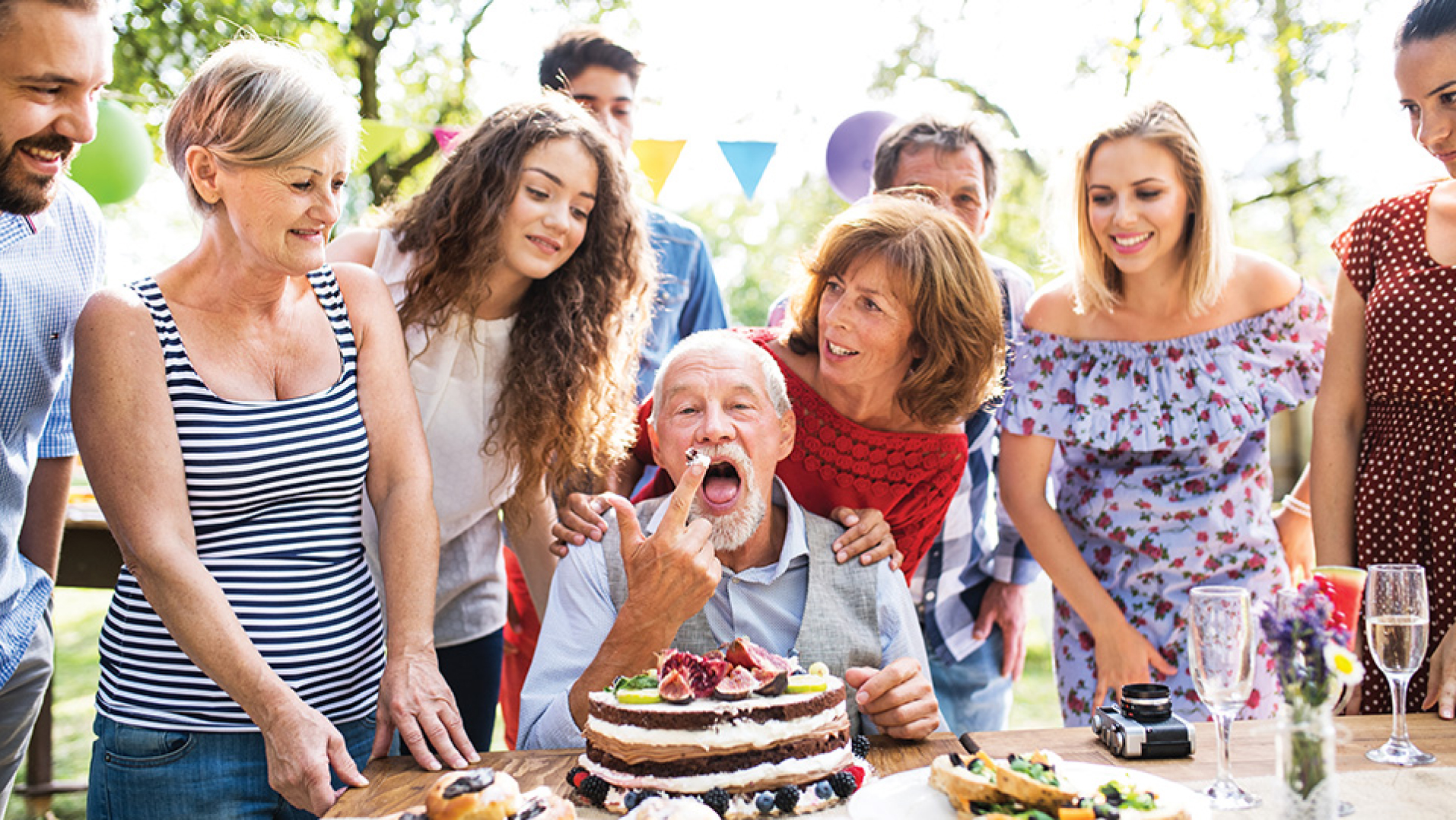 An older man surrounded by family members and loved ones at an outdoor celebration.
