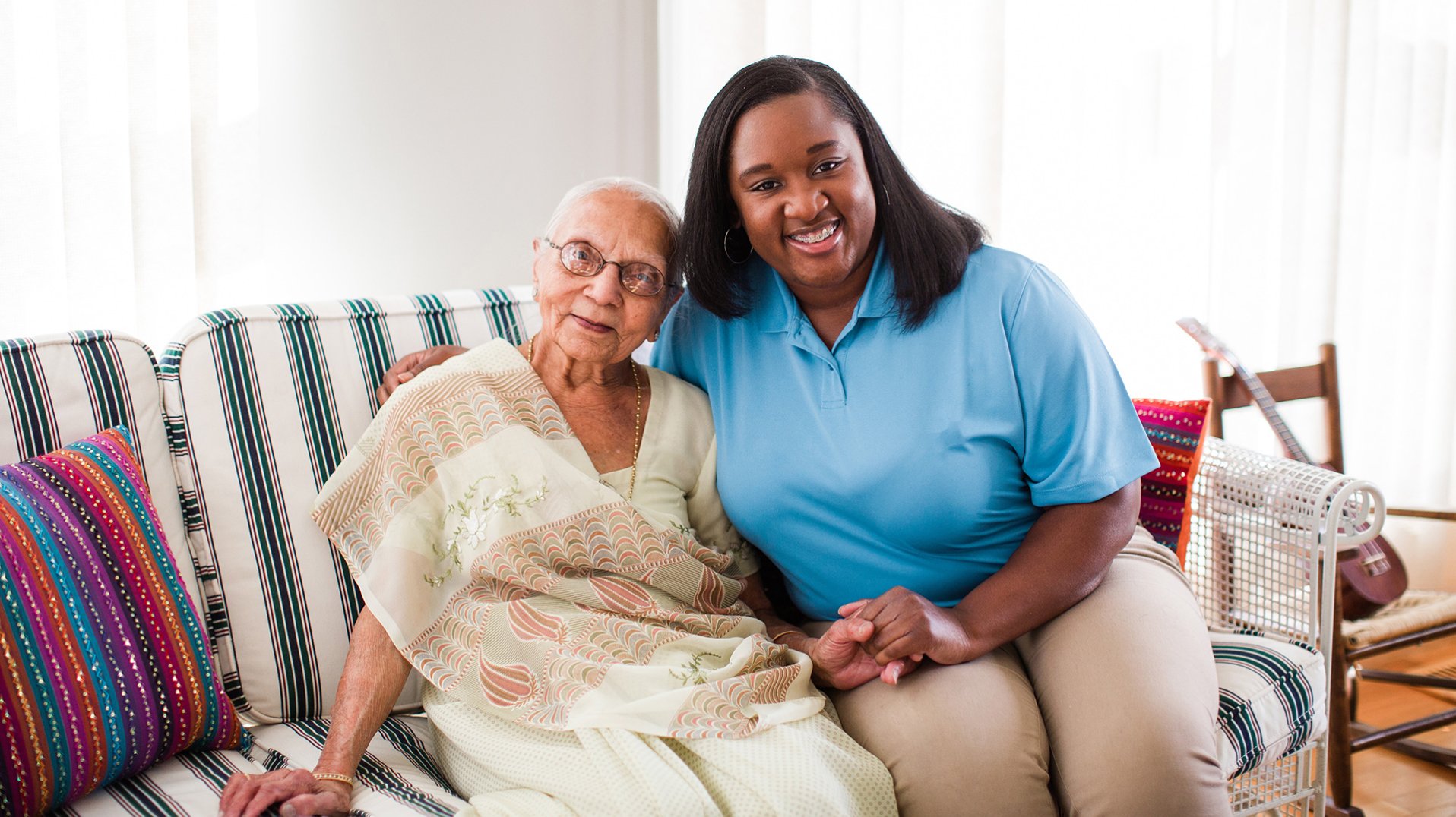 A caregiver smiling and holding hands with an elderly woman.