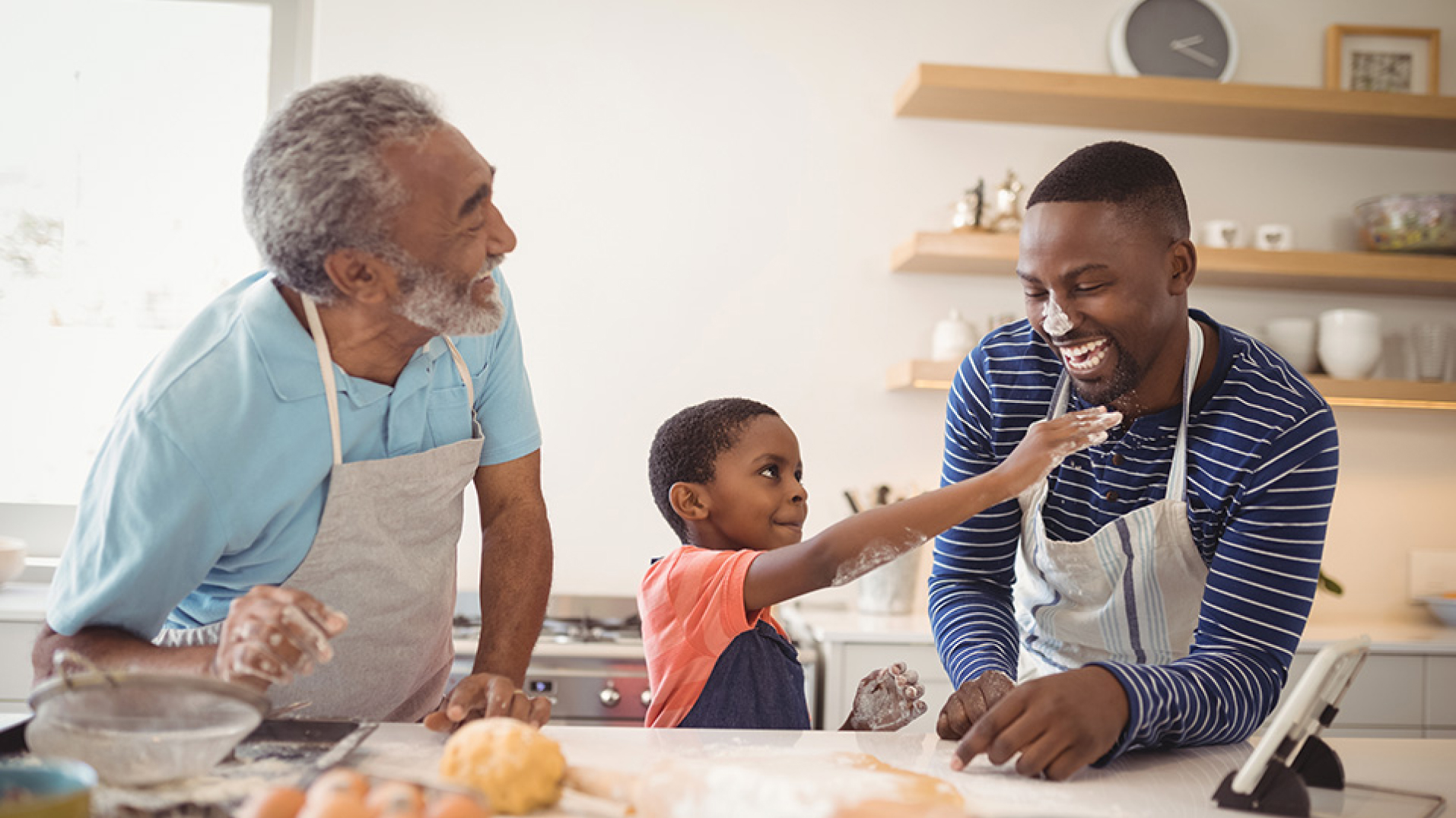 An older man, his son and his grandson baking and laughing in a home kitchen. 
