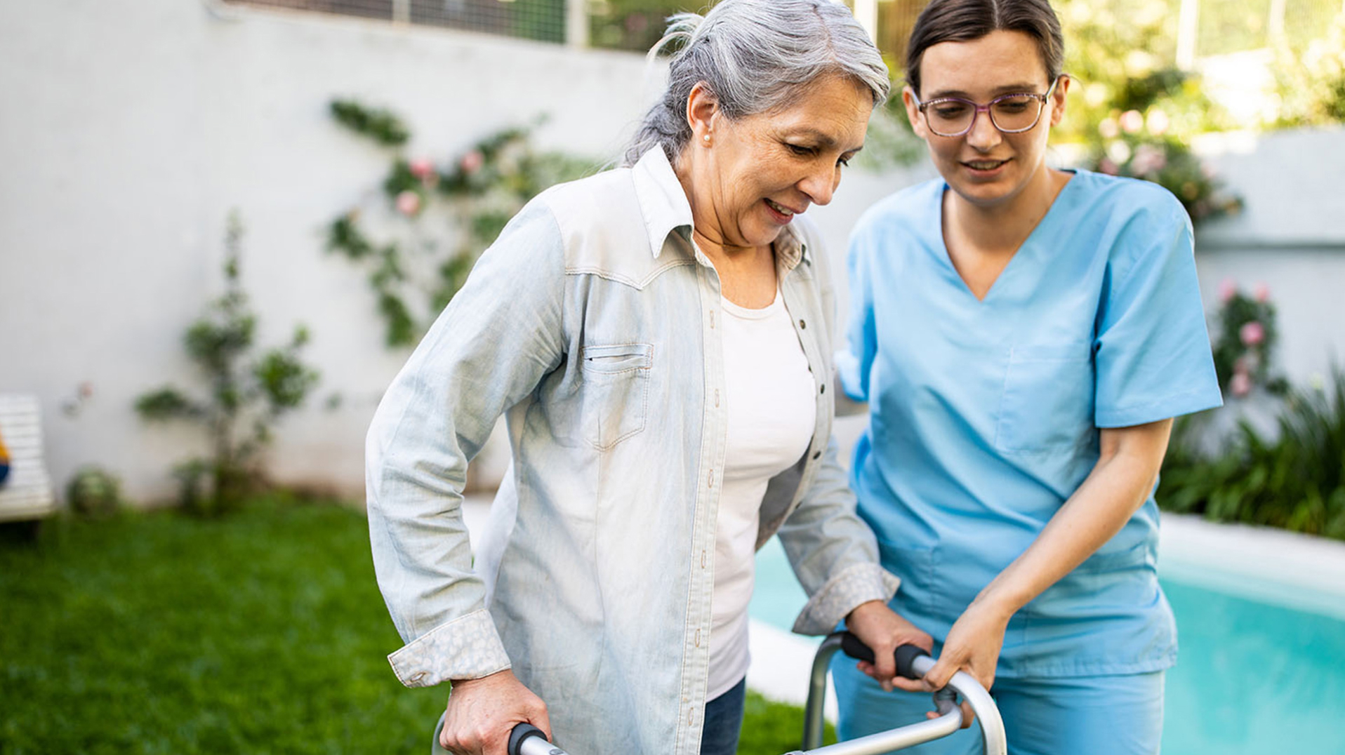 A home health physical therapist helping an elderly patient use an assistive walking device outdoors.