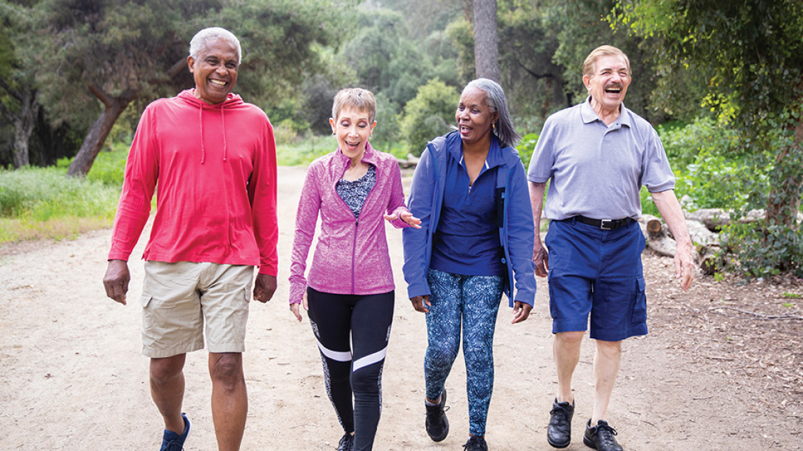 Four elderly friends smiling and laughing on an outdoor hike.